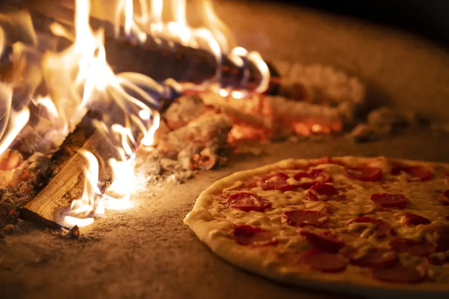 Una pizza che cuoce accanto alla fiamma del forno a legna