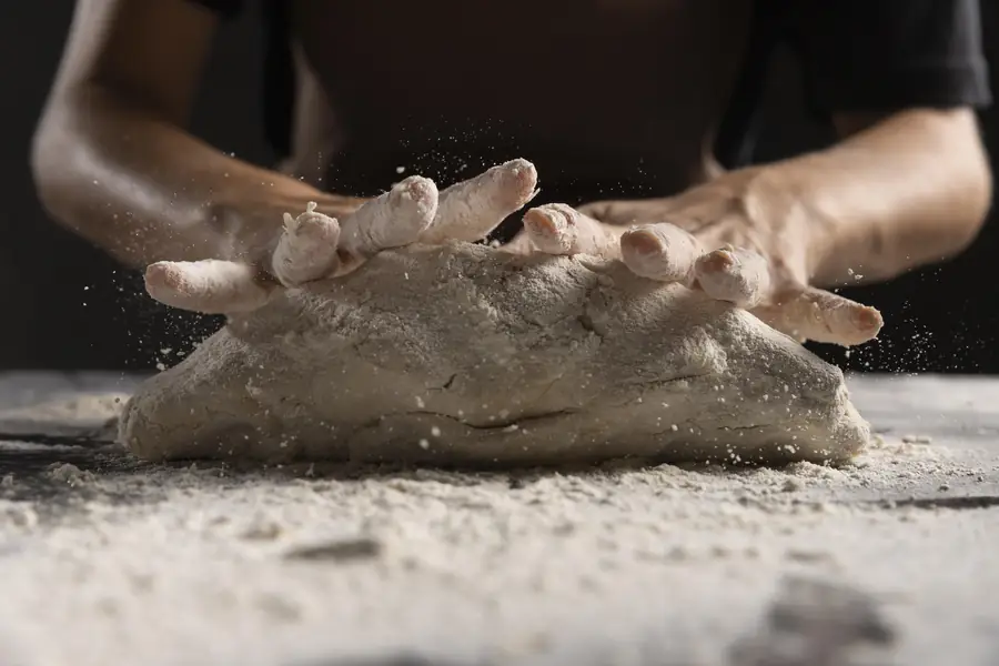 Mani che impastano la pasta della pizza su un piano infarinato