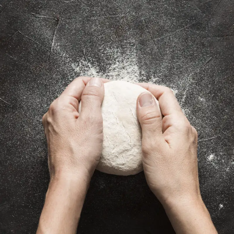 Mani che chiudono un panetto di pasta su un tavolo scuro