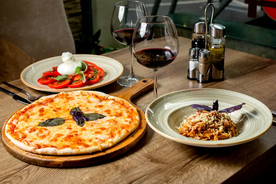 Una margherita in tavola con vino rosso, insalata e un piatto di pasta